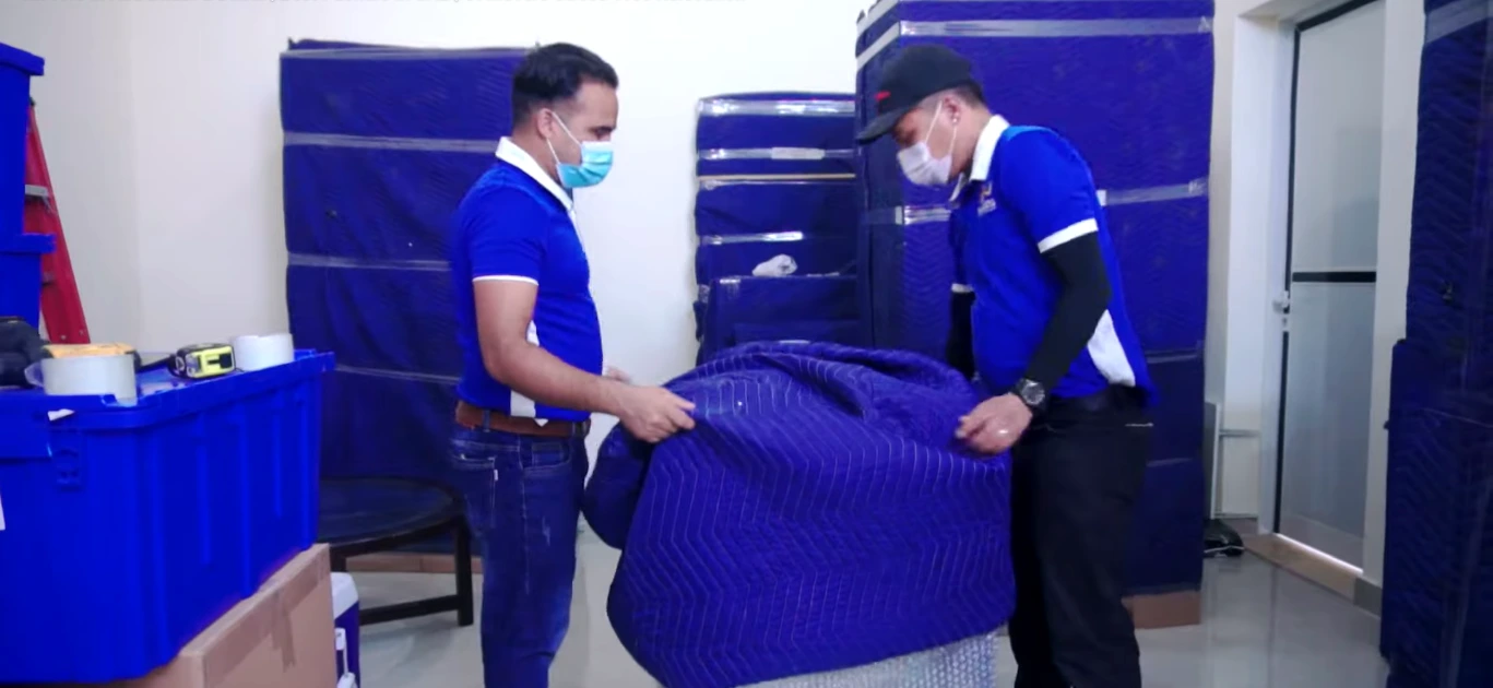 Two movers wrapping a sofa with moving blankets before loading for relocation in Dubai