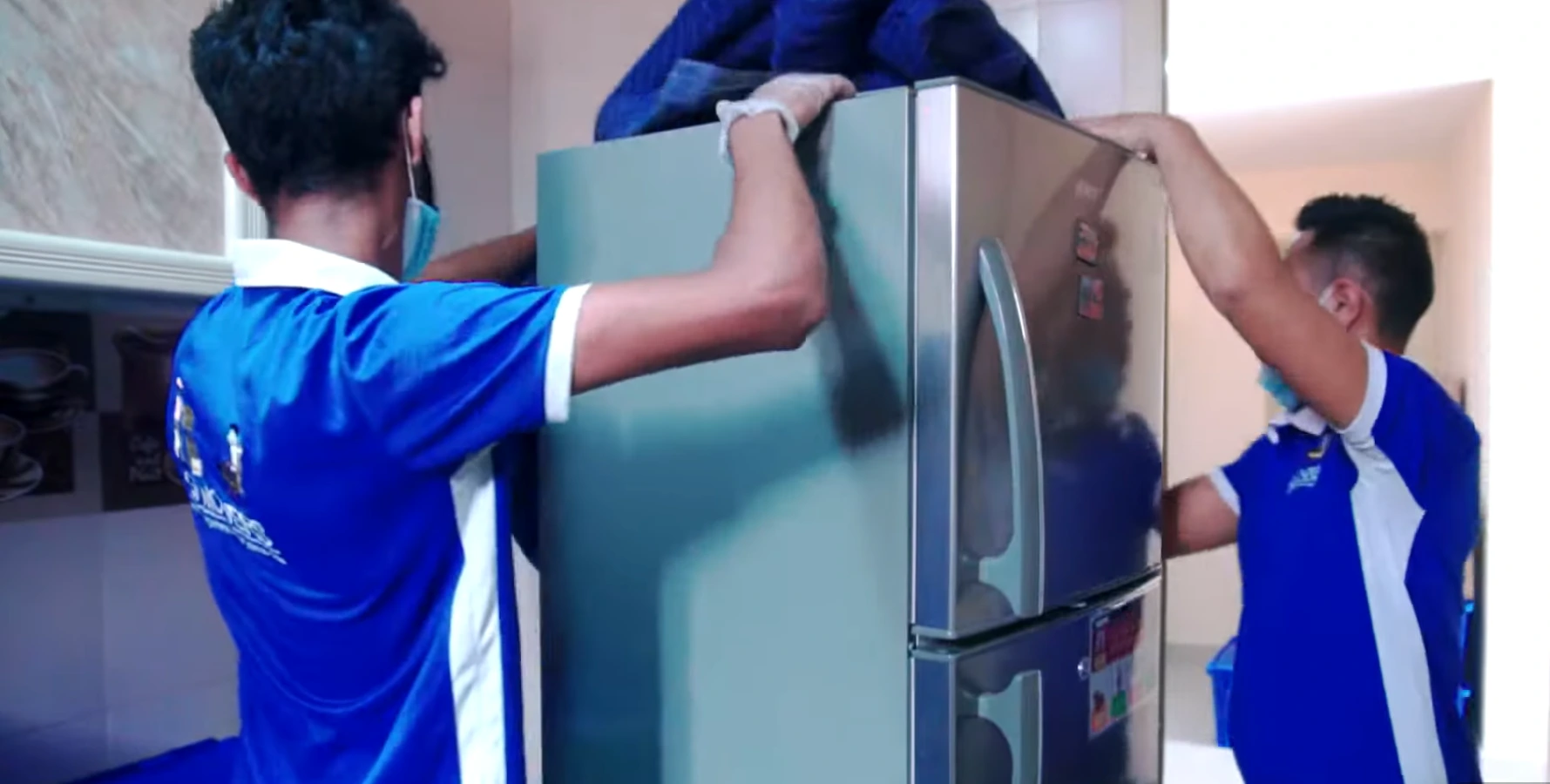 Two movers carefully relocating a stainless steel refrigerator during a residential move in Dubai